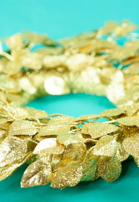 a wreath made of gold leaves on a turquoise background, zoom shot, sequins, product display photograph, detail shot