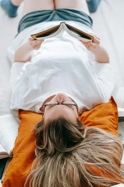 a woman laying on a bed reading a book, trending on pexels, renaissance, white and orange, dressed in a white t shirt, top down angle, reading nook