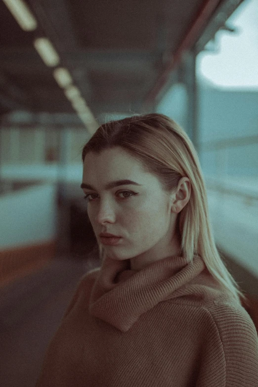 a woman standing in a train station looking at the camera, inspired by Elsa Bleda, hailee steinfeld, pale face, very grainy, blonde woman