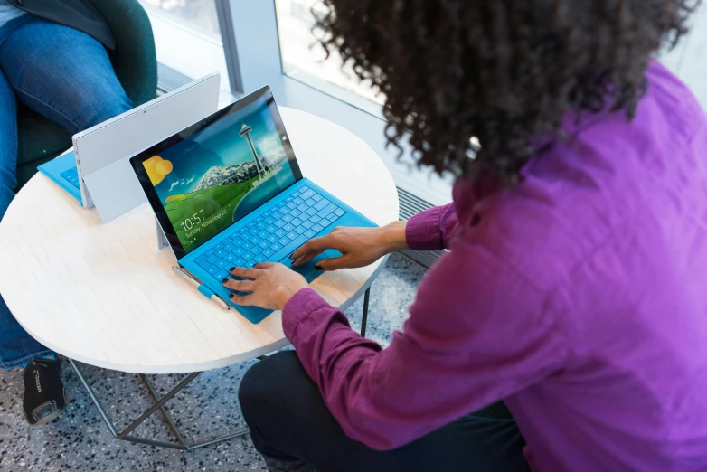 a woman sitting at a table using a laptop computer, happening, azure, using a magical tablet, on display, microsoft windows