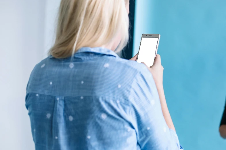 a woman standing in front of a mirror holding a cell phone, trending on pexels, wearing a light blue shirt, avatar image, blue print, no - text no - logo