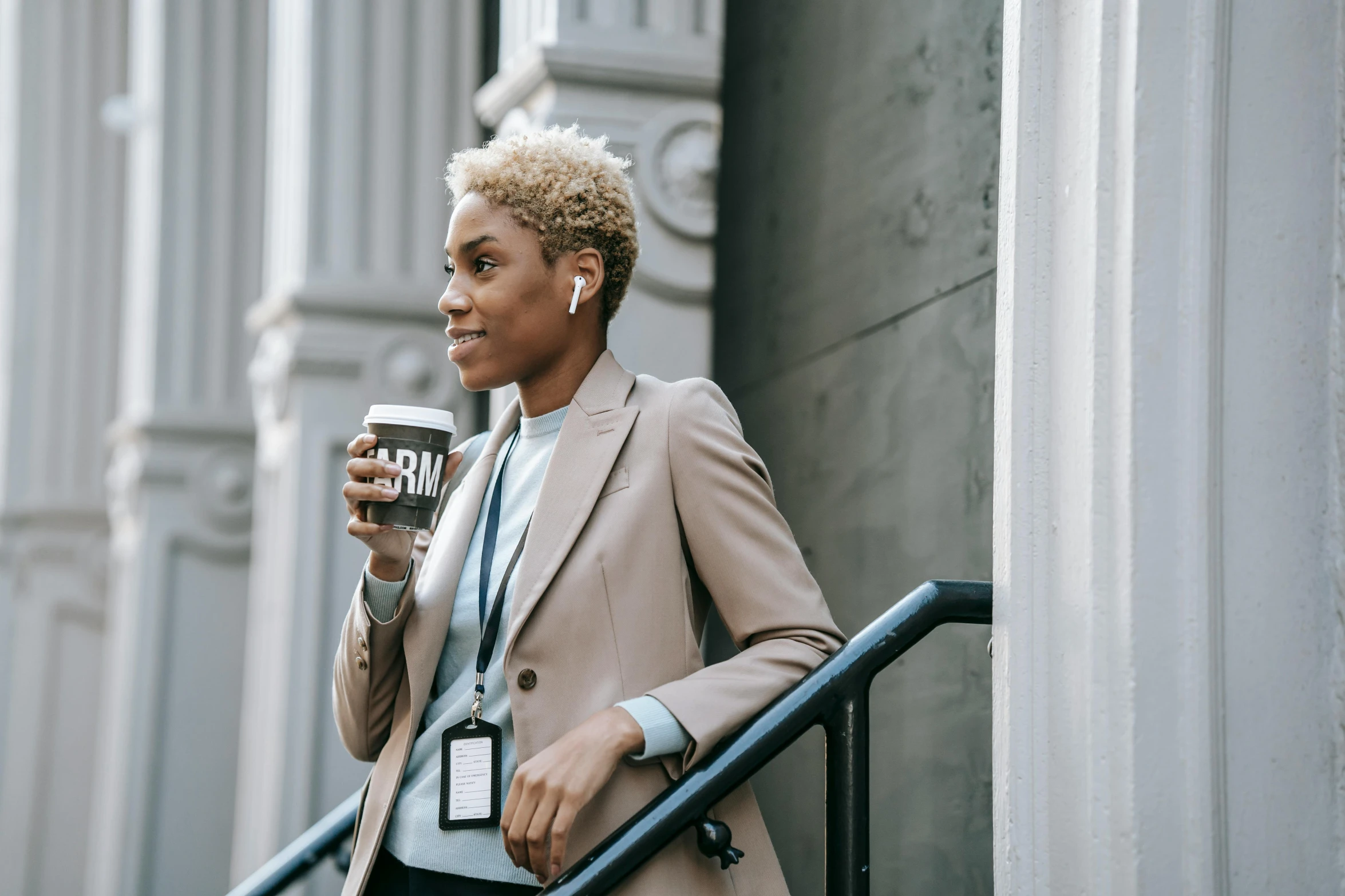 a woman in a suit holding a cup of coffee, by Carey Morris, trending on pexels, earbuds jewelry, short blonde afro, a woman walking, thumbnail