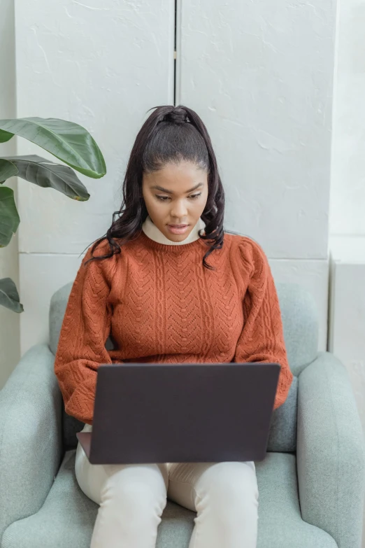 a woman sitting in a chair with a laptop, trending on pexels, renaissance, wearing a red turtleneck sweater, young black woman, orange hue, woman with braided brown hair