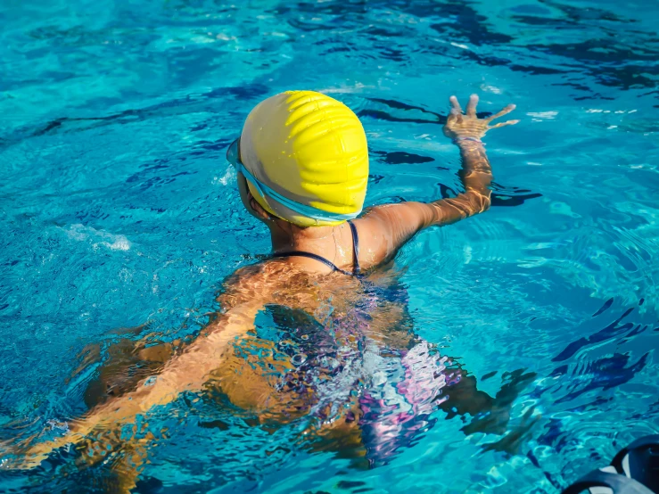 a person swimming in a pool with a yellow hat, wearing her helmet, facing away from the camera, profile image, splash image