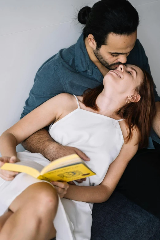 a man sitting next to a woman on top of a bed, by Lucia Peka, pexels contest winner, curled up on a book, kiss mouth to mouth, on a yellow canva, sitting on couch