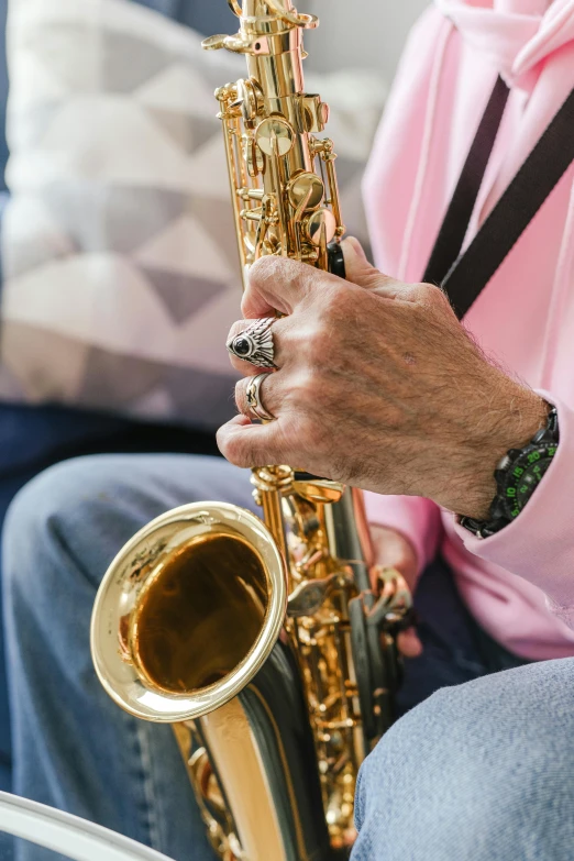 a close up of a person playing a saxophone, pink and gold, 7 0 years old, holding gold watch, seated in royal ease