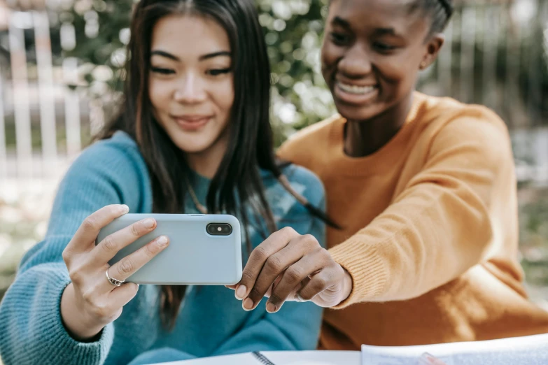 a couple of people sitting at a table with a cell phone, a picture, trending on pexels, high school girls, avatar image, environmental shot, multicoloured