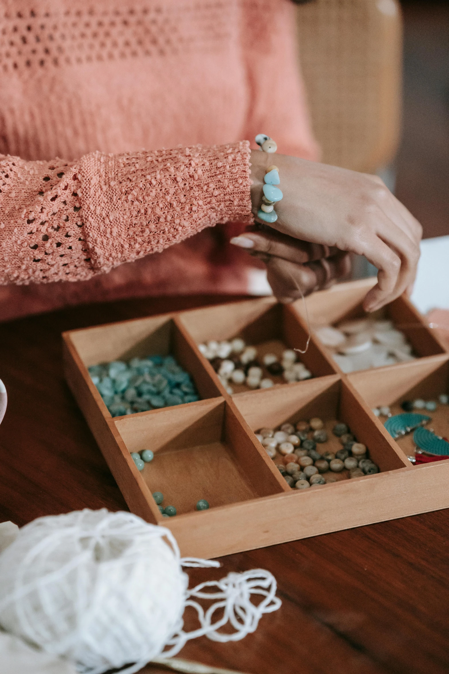 a woman sitting at a table working on a craft project, inspired by Elsa Bleda, trending on pexels, made of beads and yarn, on a wooden tray, with teal clothes, inspect in inventory image