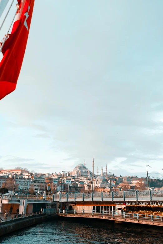 a large red flag flying over a body of water, a colorized photo, by Ismail Acar, trending on pexels, hurufiyya, city on a hillside, istanbul, instagram story, flags