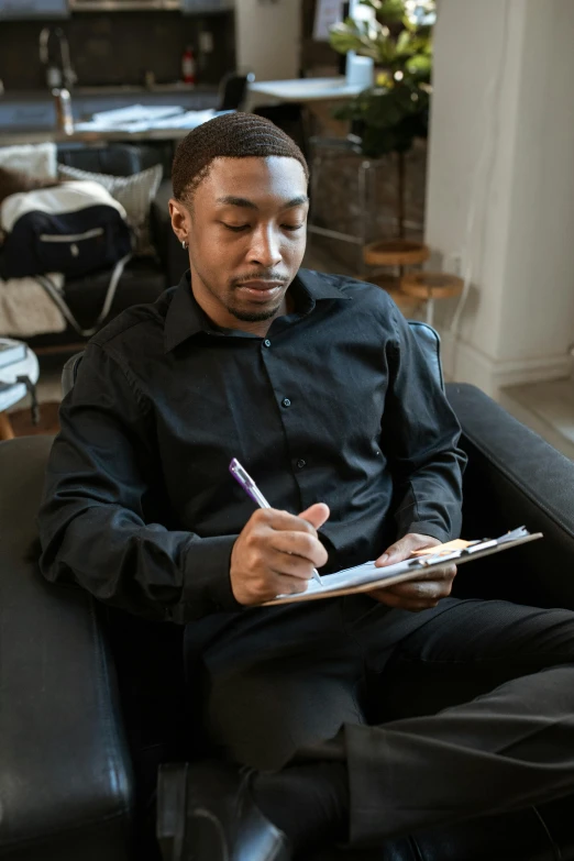 a man sitting on a couch writing on a clipboard, tailored clothing, black man, thumbnail, lgbtq