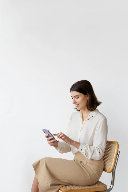 a woman sitting on a chair using a cell phone, trending on pexels, plain background, inspect in inventory image, cream colored blouse, your personal data avatar