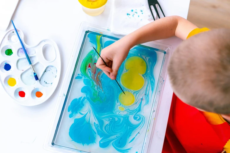 a little boy that is painting on a table, a silk screen, inspired by Helen Frankenthaler, pexels, blue translucent resin, bird eye view, multicoloured, thumbnail