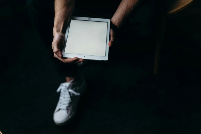 a person holding a tablet computer in their hands, an album cover, unsplash, wearing white sneakers, the lighting is dark, blank stare”, thumbnail