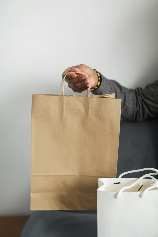 a woman sitting on a couch holding a shopping bag, by Ben Zoeller, pexels contest winner, renaissance, hand on table, man walking, brown paper, cutlery