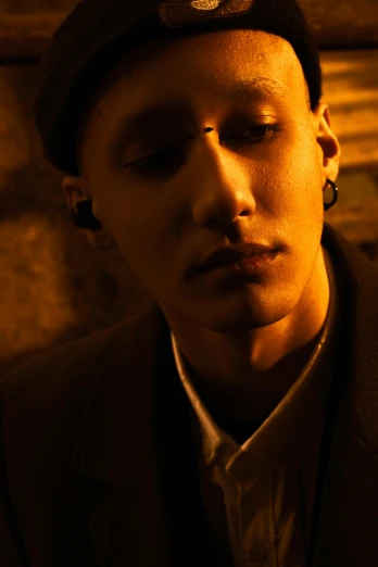 a close up of a person wearing a hat, an album cover, inspired by Dmitry Levitzky, young handsome pale roma, korean film noir, shaved sides, warm glow from the lights