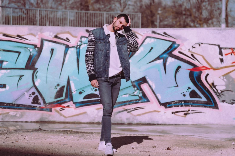 a man talking on a cell phone in front of a graffiti wall, an album cover, inspired by Antoine Wiertz, pexels contest winner, graffiti, outfit : jeans and white vest, avatar image, épaule devant pose, wearing a jeans jackets