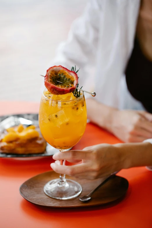 a person sitting at a table with a glass of orange juice, trending on pexels, renaissance, passion fruits, cocktail bar, chilean, standing elegantly