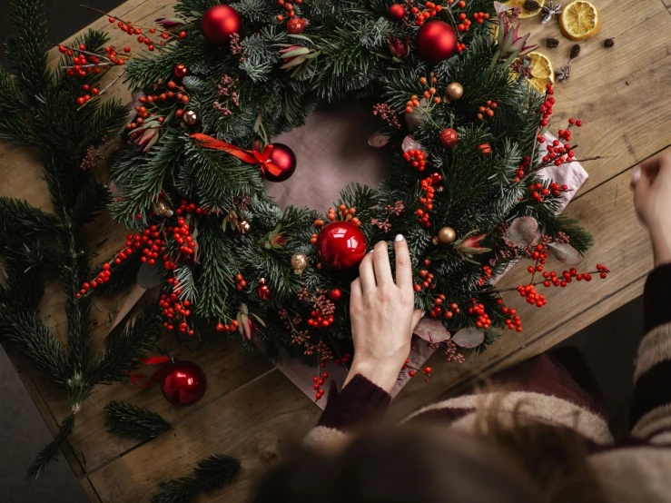 a woman decorating a christmas wreath on a wooden table, pexels contest winner, hurufiyya, thumbnail, circle, red adornments, 🦩🪐🐞👩🏻🦳