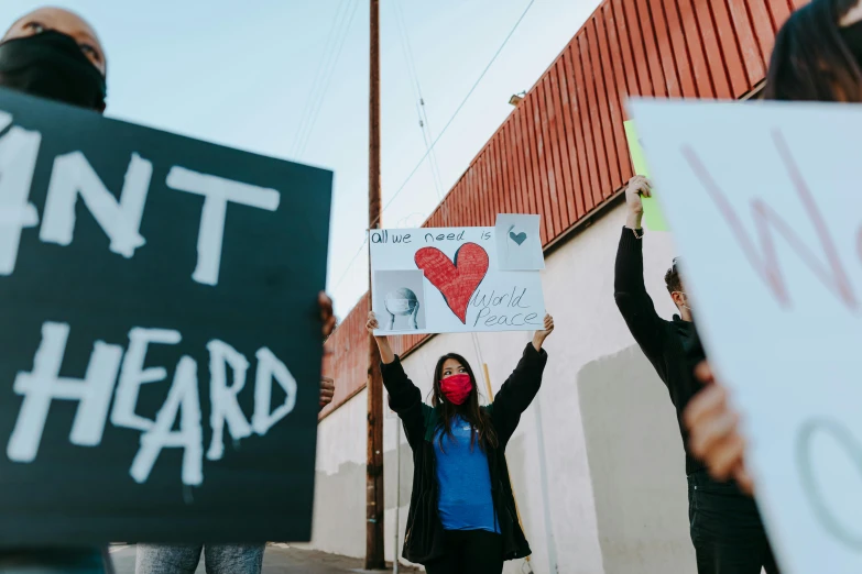 a group of people holding signs in front of a building, by Julia Pishtar, trending on pexels, sots art, (heart), coward, rafeal albuquerque, eyardt