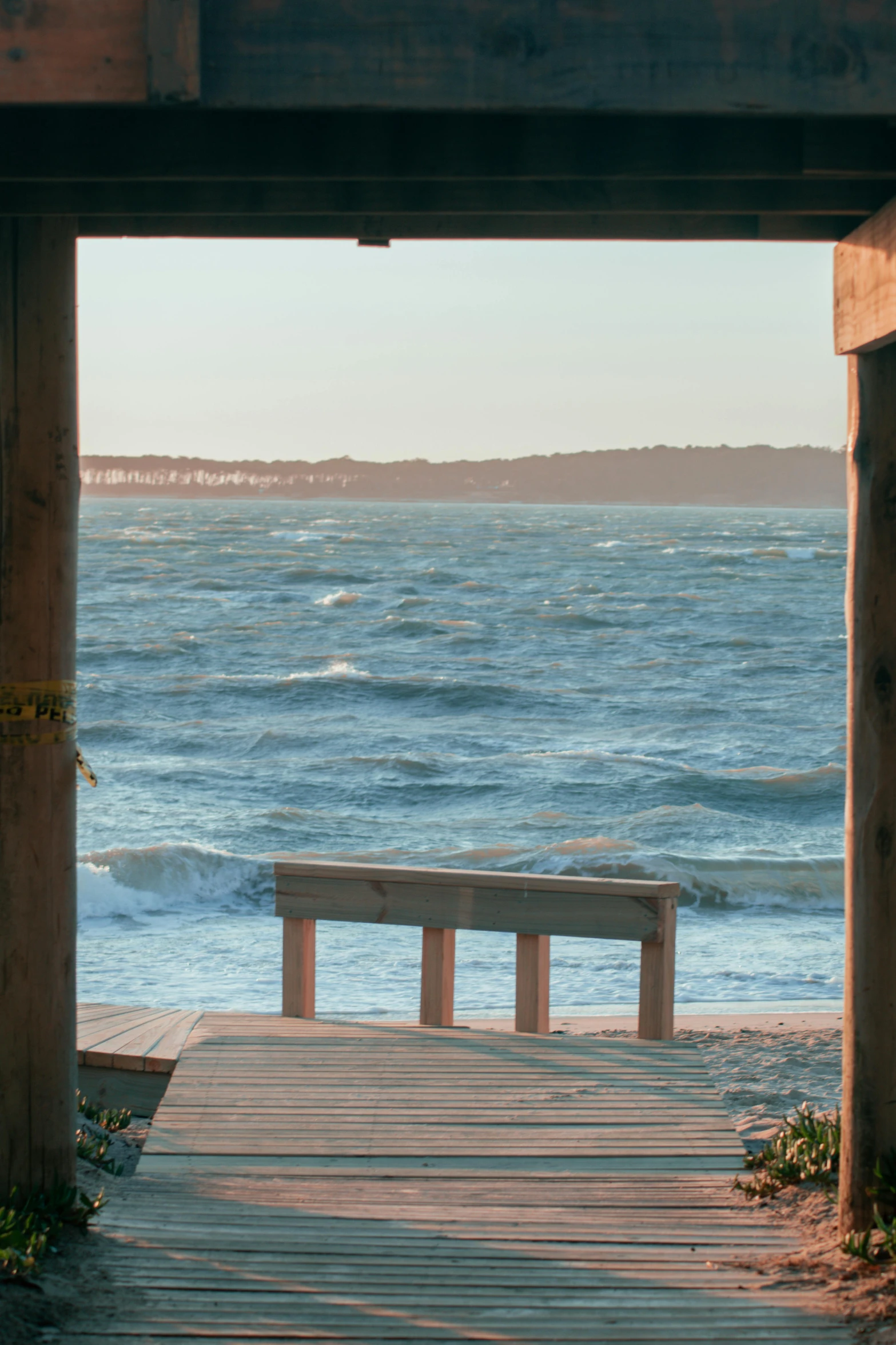 a bench sitting on top of a wooden walkway next to the ocean, a picture, high winds, looking through a portal, espoo, beach pic