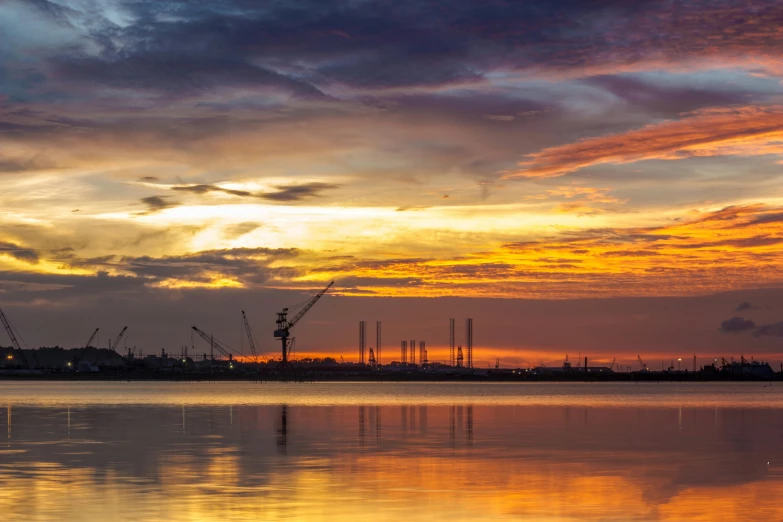 a large body of water under a cloudy sky, a picture, pexels contest winner, romanticism, industrial colours, sunset panorama, cranes, award winning landscape photo