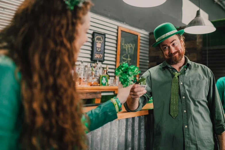 a man standing next to a woman at a bar, by Meredith Dillman, pexels contest winner, hurufiyya, four leaf clover, green flags, 🍸🍋, pouring