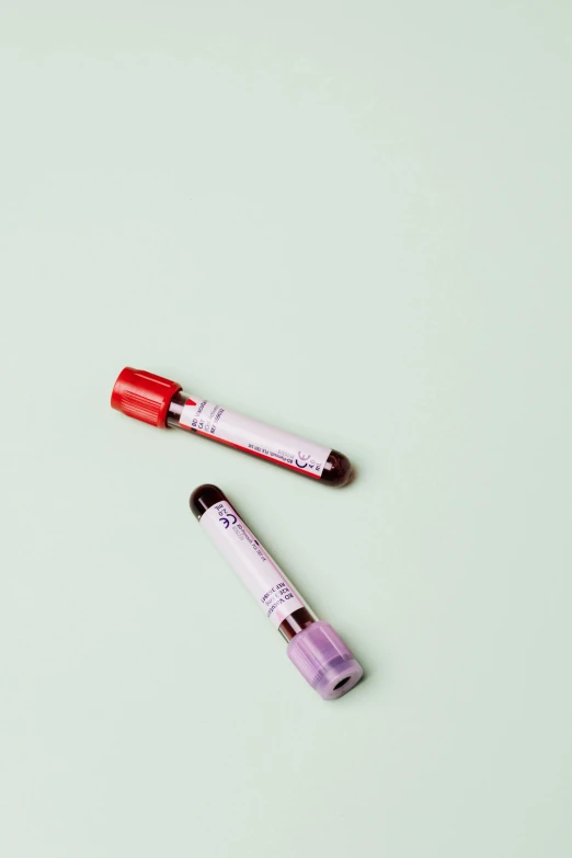 two tubes of blood sitting next to each other, by Nicolette Macnamara, products shot, cool and bright tint, medical labels, on a pale background