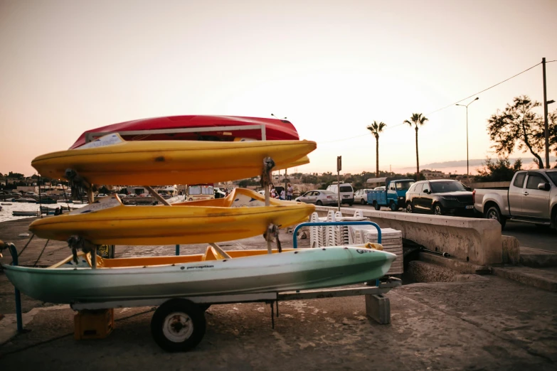 several kayaks stacked on top of each other in a parking lot, unsplash, les nabis, at the beach on a sunset, small boat, profile image, with a roof rack