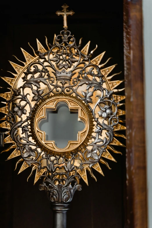 a close up of a metal object with a cross on it, pinterest, baroque, inside mirror, intricate light, brown, halo of light