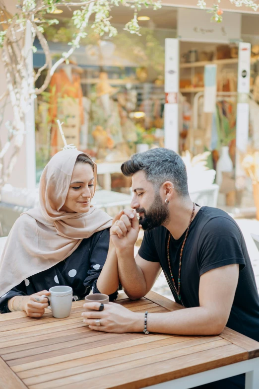 a man and a woman sitting at a table, pexels contest winner, young middle eastern woman, scarf, holding hand, cute scene