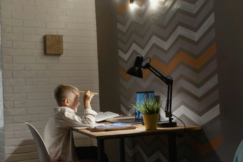 a young boy sitting at a desk in front of a laptop computer, inspired by Leo Leuppi, pexels contest winner, light and space, small and cosy student bedroom, rgb wall light, cinematic lighting h 704, demur