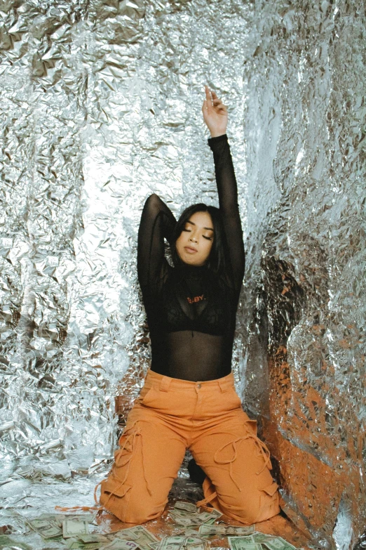 a woman standing in front of a waterfall, an album cover, by Robbie Trevino, trending on pexels, visual art, silver space suit, orange, studio shoot, sun yunjoo