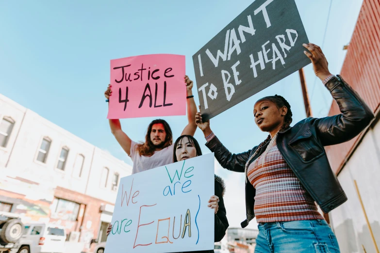 a group of people holding signs on a city street, by Julia Pishtar, trending on pexels, essence, polychromatic, justice, four