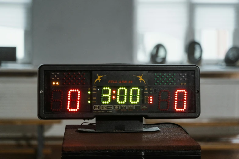 a digital clock sitting on top of a wooden table, in the high school gym, black and yellow and red scheme, with a star - chart, running lights