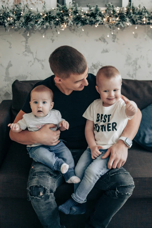 a man sitting on a couch holding two babies, by Julia Pishtar, pexels contest winner, buzz cut, alexey egorov, shirt, celebrating