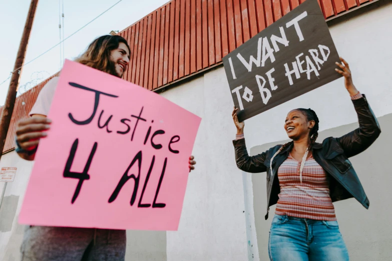 two women holding signs in front of a building, trending on pexels, justice, diverse, 2045, an ultra realistic