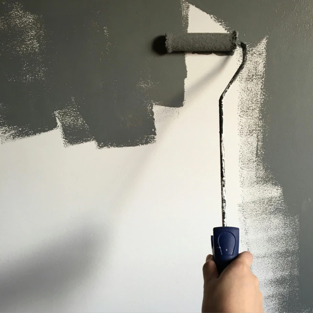 a person using a paint roller to paint a wall, a minimalist painting, inspired by Julio Larraz, pexels contest winner, arbeitsrat für kunst, grey, background image, vantablack wall, painting of