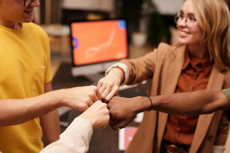 a group of people putting their hands together, trending on pexels, happening, avatar image, holding a staff, professional image, brown