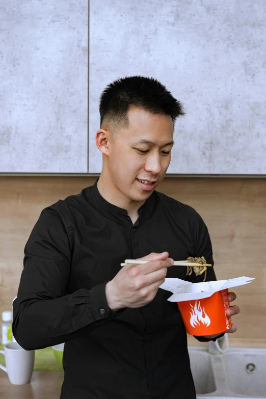 a man standing in a kitchen holding a container of food, inspired by Reuben Tam, burning wings, eating noodles, profile photo, darren quach