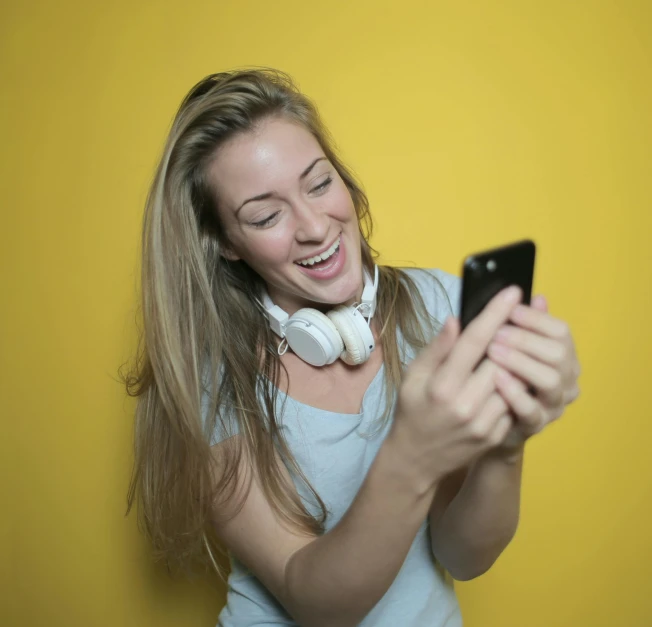 a woman smiles while looking at her cell phone, pexels contest winner, happening, yellow and black, avatar image, blonde, headset