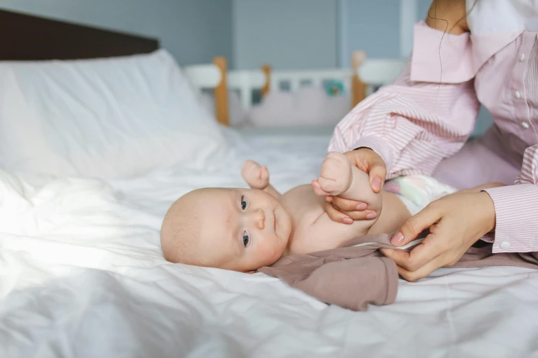 a woman holding a baby on top of a bed, unsplash, knees upturned, pale - skinned, healthcare, full colour