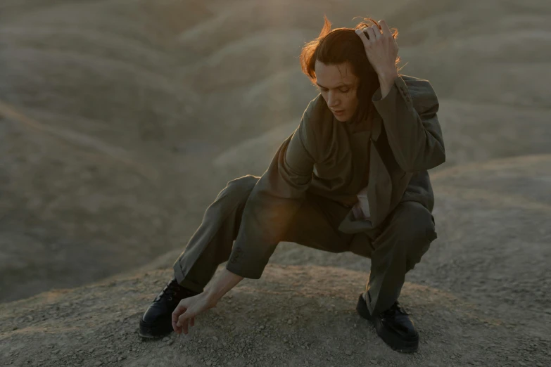 a man sitting on top of a large rock, an album cover, inspired by Anna Füssli, antipodeans, standing in a desert, in an action pose, sigourney weaver, cinematic outfit photo