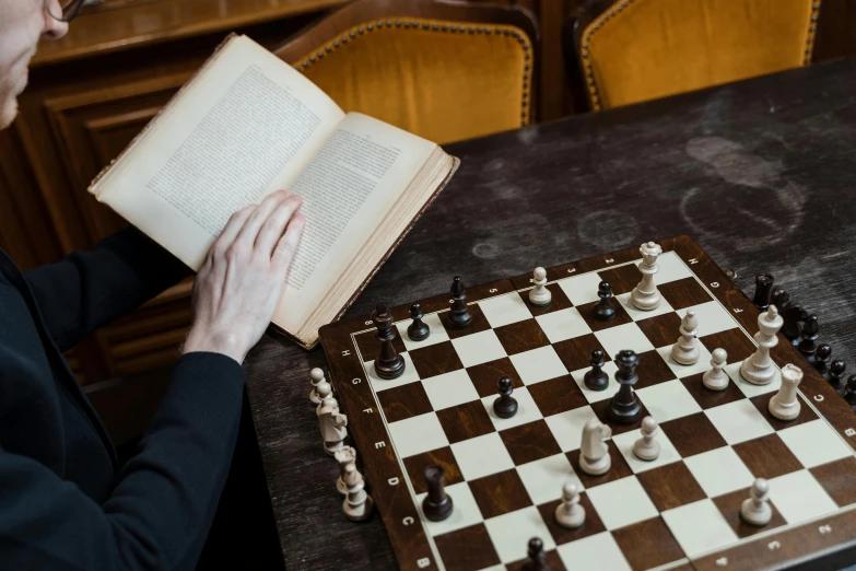 a man sitting at a table playing a game of chess, by Carey Morris, pexels contest winner, with one vintage book on a table, inside a grand, private school, board games on a table