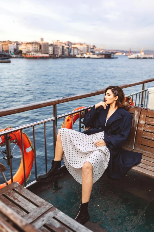 a woman sitting on a bench next to a body of water, polka dot, wearing dark maritime clothing, istanbul, trending on imagestation