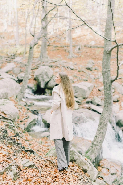 a woman standing by a stream in the woods, trending on pexels, light brown trenchcoat, young with long hair, thoughtful ), low quality photo