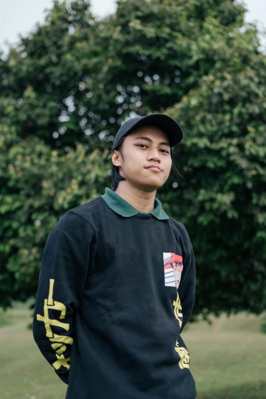 a man standing on top of a lush green field, inspired by Eddie Mendoza, unsplash, realism, wearing a black hoodie, south east asian with round face, wearing a baseball cap backwards, formal attire