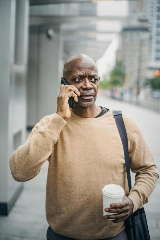 a man talking on a cell phone while holding a cup of coffee, blind brown man, aging, 2019 trending photo, walking confidently