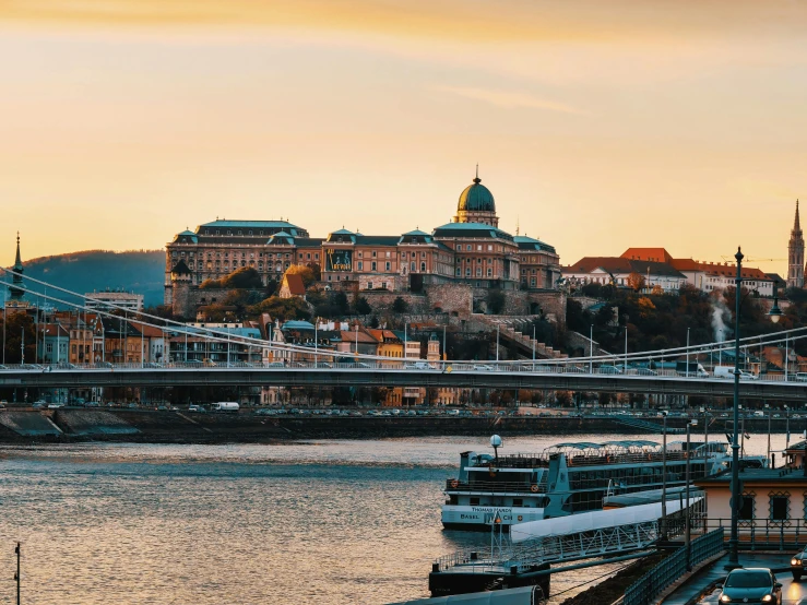 a large boat sitting on top of a river next to a bridge, by Adam Szentpétery, pexels contest winner, grand budapest hotel, sunset panorama, hills in the background, 🚿🗝📝
