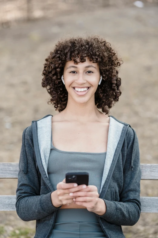 a woman sitting on a bench holding a cell phone, curly middle part haircut, earbuds, mobile app, black