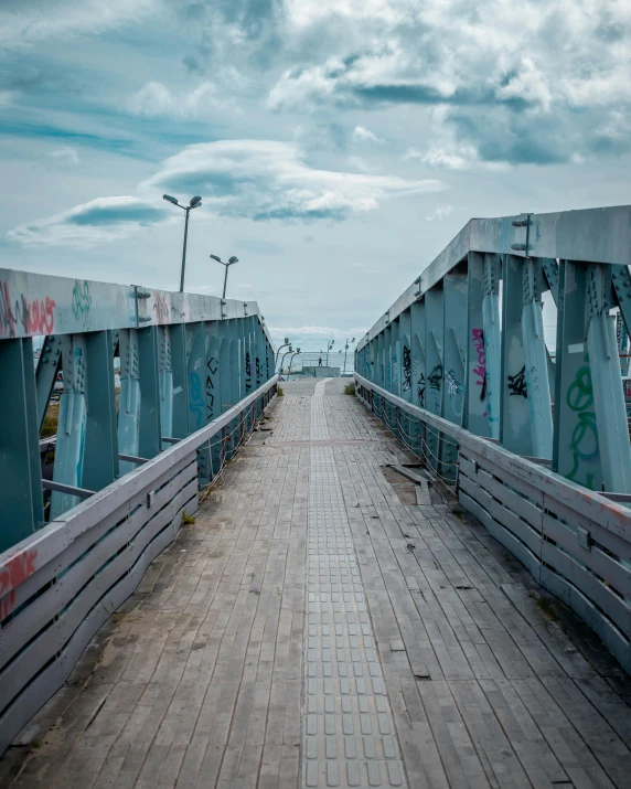 a long wooden bridge with graffiti on it, pexels contest winner, shades of blue and grey, lgbtq, seaview, brutalist city